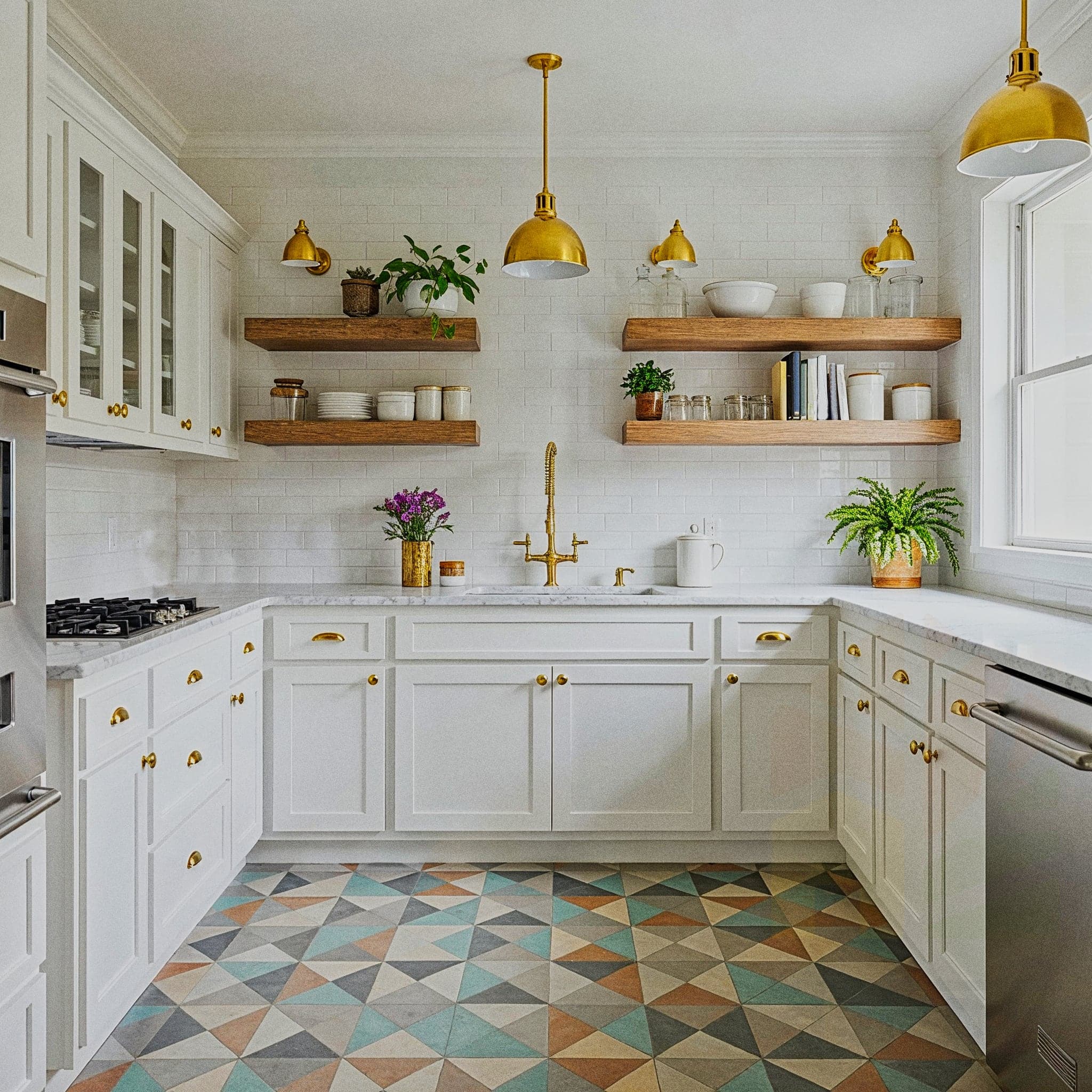 A sophisticated kitchen with a Midcentury Modern design, featuring walnut cabinets with sleek handles, a white countertop with a retro toaster, and a tiled backsplash with geometric patterns. The room includes open shelves with vintage glassware, a tulip-shaped pendant light with a white shade, and a small dining table with curved legs. Large windows with sheer curtains allow natural light to enhance the light wooden floor and teal accent wall, creating a stylish and functional cooking atmosphere.